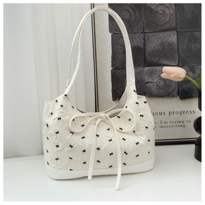 Détail du sac cabas beige avec broderie nœud et ruban à pompons longs sur tissu bullé