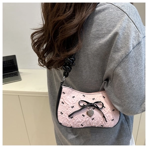 Detail view of pink embossed handbag with black bow patterns and metal heart pendant