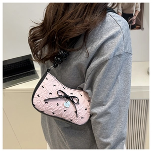 Detail of pink embossed underarm bag featuring black bow patterns and silver heart charm