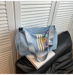 Detail view of light blue nylon sports bag featuring three white stripes and star charm