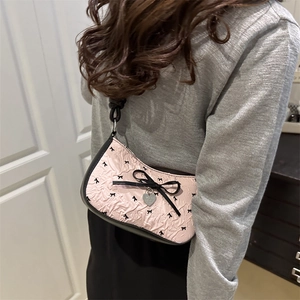 Pink bow underarm bag with black ribbon patterns and heart charm on a shoulder strap