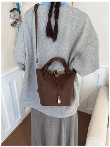Detail of a dark brown lychee leather bucket bag with a metal lock and shoulder strap