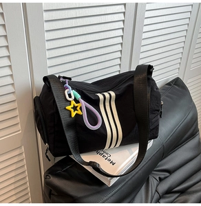 Detail of black cylinder sports bag featuring three white stripes and star charm