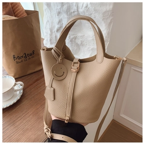 Close-up of beige lychee grain bucket bag with smiley charm and crossbody strap details