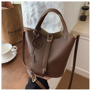 Detail of dark brown lychee grain leather bucket bag with metal lock and smile charm