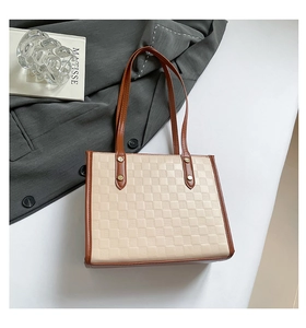 Detail of checkered embossed tote bag with brown leather handles and gold rivets