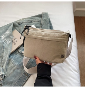 Close-up of beige nylon crossbody bag with multi-layer zippers and wide strap on white sheets
