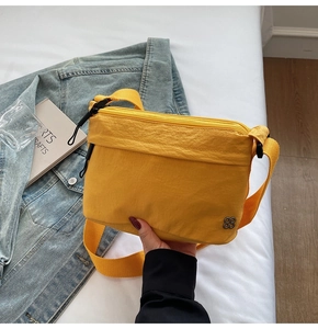 Detail of yellow nylon crossbody bag featuring metallic floral logo and layered zippers