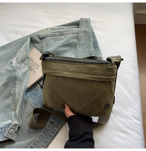 Close-up of army green nylon crossbody bag with clover logo on a white bed sheet