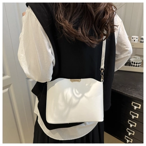 Upper body view of a woman wearing a white leather crossbody bag with wavy edge design