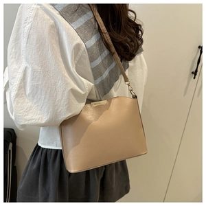 Model wearing a light khaki shoulder bag featuring gold metal hardware and a sleek design