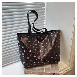 Détail du sac cabas noir avec motifs de nœuds roses et fleurs sur un rebord de fenêtre