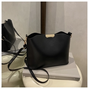 Detail of a black leather bucket bag with gold metal trim displayed on a cream stool