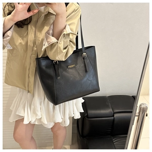 Classic black leather tote bag with gold hardware worn by a model in casual attire