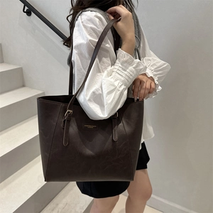 Classic dark brown leather tote bag with gold hardware shown on female model shoulder