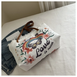 Detail van canvas draagtas met bloemenborduurwerk, gerafelde randen en leren riem