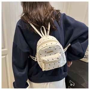 Detail view of mini white backpack with bird print and gold Fashion logo on model