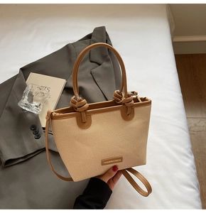 Détail d'un grand sac cabas en paille beige avec garniture en cuir brun et anses nouées