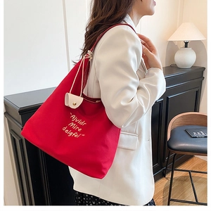 Detail of red canvas tote bag with yellow embroidery and a mini decorative cream pouch