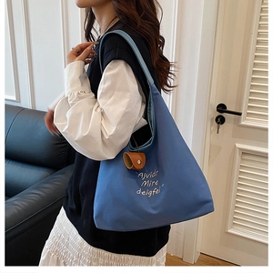 Blue canvas tote bag detail with embroidery and leather charm shown on shoulder