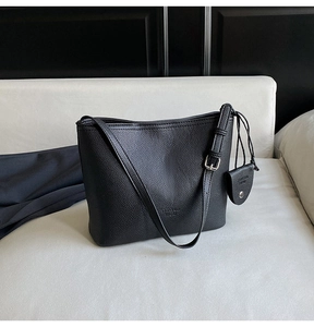 Detail of black lychee grain leather bucket bag with silver hardware on a soft sofa