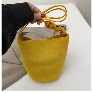 Détail du sac seau jaune en daim mat avec poignée nouée décorative et texture douce