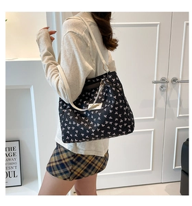 Detail of large black tote bag with white bow pattern and adjustable cream shoulder strap