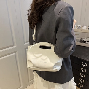 Elegante borsa a secchiello bianco crema con manico traforato e tracolla su blazer grigio