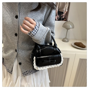 Dettaglio della mini borsa nera lucida con bordo in pizzo bianco e fiocco decorativo
