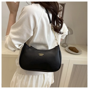 Détail d'un sac sous le bras en cuir grainé noir avec chaîne dorée porté par un mannequin