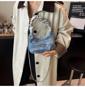 Detail of blue denim crescent bag with silver butterfly charms and ruffled handle