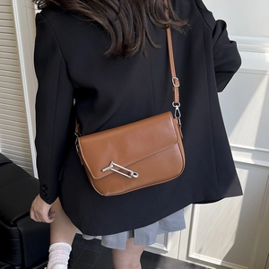 Minimalist caramel saddle bag with designer silver pin buckle on white wall background