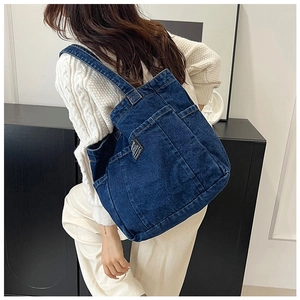Close-up of a dark blue denim tote bag showing diagonal texture and a front storage pocket