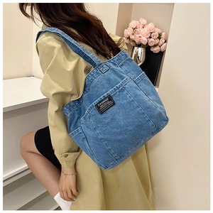 Macro detail of dark blue denim tote bag featuring dual front pockets and fashion patch