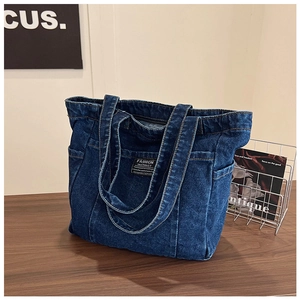 Detail of dark blue washed denim tote bag showing side pocket and woven brand label