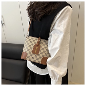 Detail view of beige plaid bucket bag with brown leather trim worn by model
