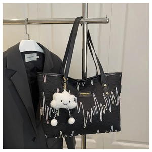 Detail of black embroidered canvas tote with 3D texture and cloud charm accessory