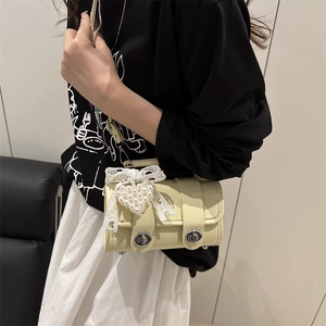 Cremegelbe Boston-Tasche mit Perlenherz und Spitzenschleife an einem Modell gezeigt