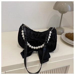Détail du sac à main noir à nœud avec anse en perles sur une table élégante