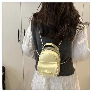 Dettaglio di un mini zaino giallo con fiocco decorativo, pizzo e spalline a catena