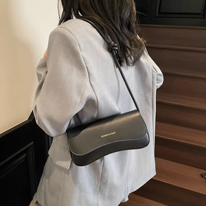 Minimalist black crescent underarm bag with gold lettering shown on a model's shoulder