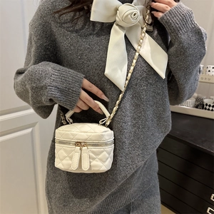 White mini quilted box bag with gold chain strap worn by a model in a modern interior