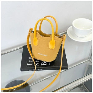 Mini borsa a secchiello giallo senape con testo moda poggiata su un libro nero