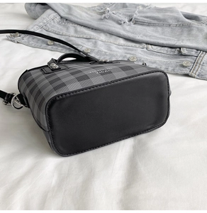 Détail du sac seau à carreaux gris avec poignée en cuir noir sur tissu blanc
