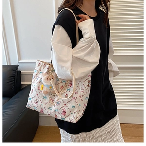 Detail of white tote bag with cute cartoon prints, plush bunny charm and golden chain