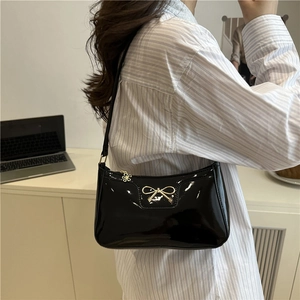 Glossy black patent leather underarm bag with gold bow ornament and flower pendant