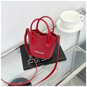 Dettaglio della mini borsa a secchiello in pelle scamosciata rossa su libro nero