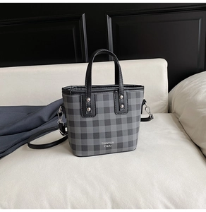 Détail du sac seau à carreaux gris avec poignées en cuir et accents de rivets métalliques