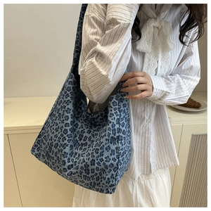 Sac fourre-tout en toile à imprimé léopard bleu porté à l'épaule dans un décor intérieur