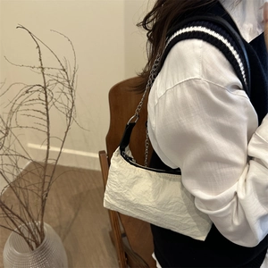 Sac hobo blanc plissé en toile avec chaîne argentée porté par un modèle en intérieur